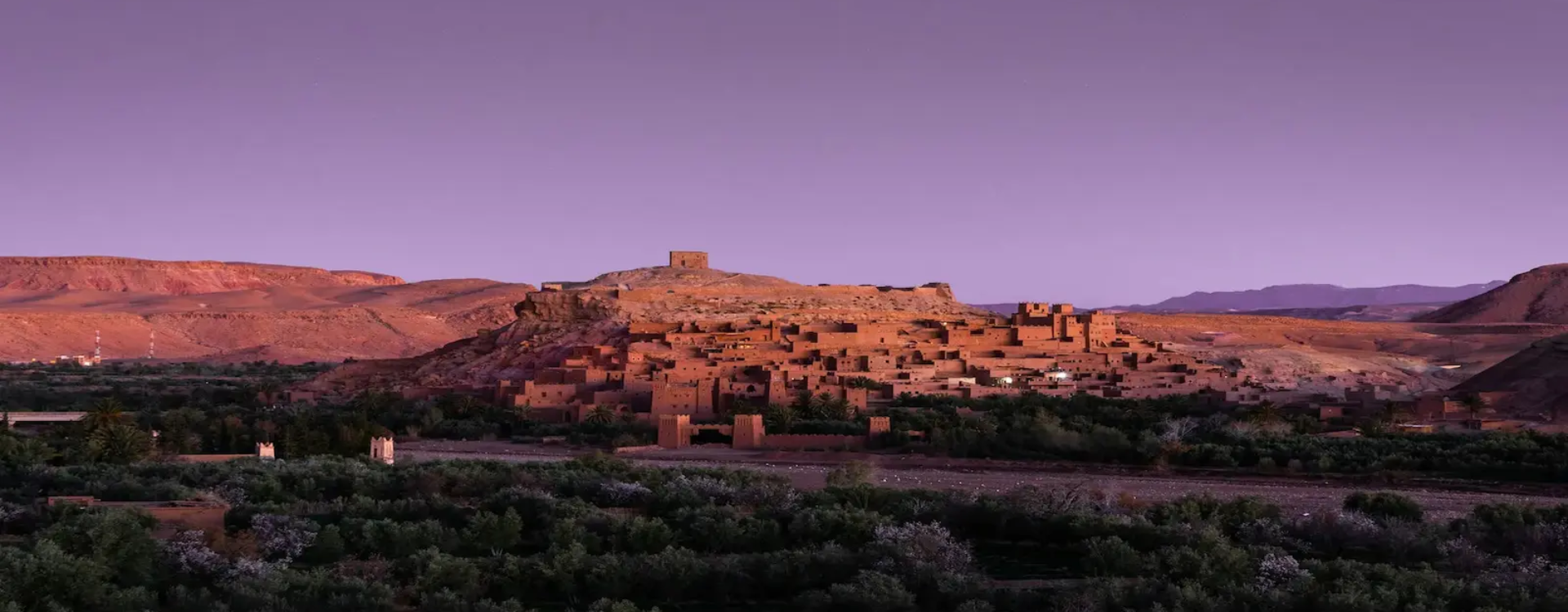 Ait Ben Haddou Kasbah in Morocco at sunset with desert landscape and Atlas Mountains